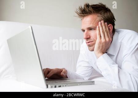 Businessman working remotely lying on white sofa using his laptop computer Stock Photo