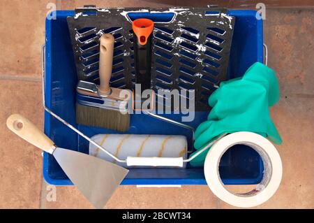 Top view of a paint bucket in which there is a painter's brush and roller, along with gloves and a scraper to carry out the decoration work Stock Photo