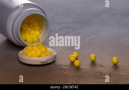 Textured blue gray and golden background with opened white plastic bottle lying on side and full of round yellow pills of Vitamin C. Few pills are sca Stock Photo
