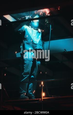 Profesional welder in protective uniform and mask welding metal construction in the industrial object Stock Photo
