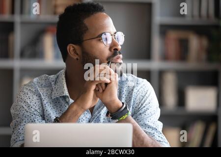 Pensive biracial man lost in thoughts dreaming at workplace Stock Photo