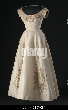 A cream silk faille dress with embroidered floral appliqué decorations  designed by Ann Lowe. The dress has a bodice with cap sleeves, a scoop neck  front, and a deep scoop neck back.