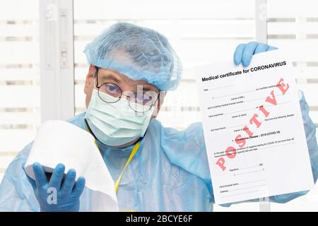 Doctor in protective suit holding positive medical certificate at coronavirus - covid 19 and offers toilet paper. The Laboratory examination of blood Stock Photo