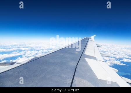 Airplane window view showing wing of plane flying above the clouds. Stock Photo