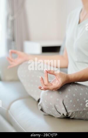 Young woman keeping hands in shuni mudra when meditating on sofa at home Stock Photo