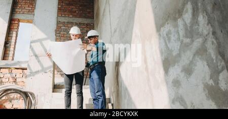 Two caucasian engineers with helmet looking at the building plan posing in a new apartment Stock Photo