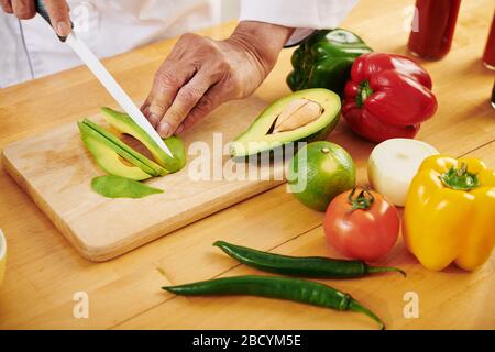 Hands of man cutting avocado and other fresh vegetables in thin slices Stock Photo