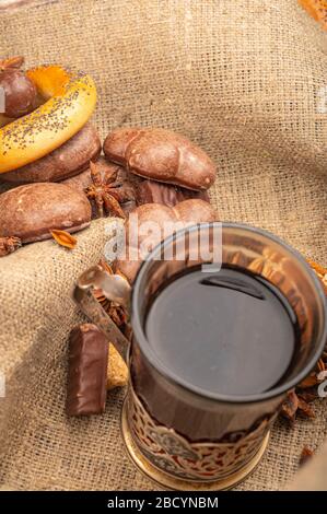 Cut glass with tea in a vintage Cup holder, star anise, cookies, gingerbread and chocolate on a background of rough homespun fabric. Close up Stock Photo