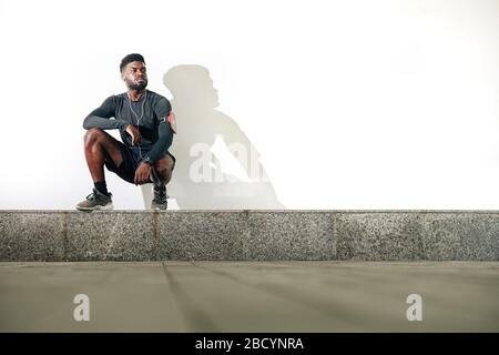 Serious confident young Black sportsman sitting on haunches on kerb Stock Photo