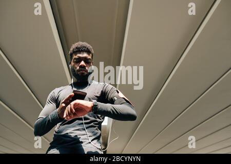 Serious Balck sportsman synchronizing health applications in smartphone and smartwatch before training Stock Photo