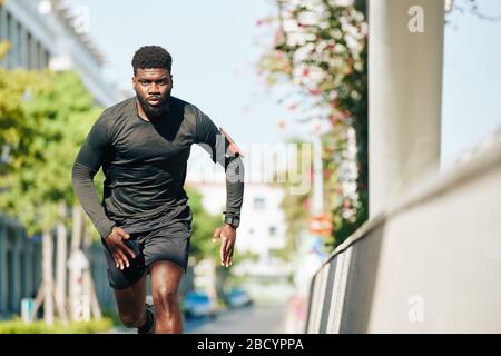 Serious concentrated Black young man running in the street when training for marathon Stock Photo