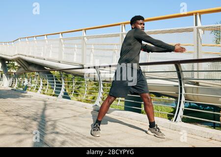 Serious young Black sportsman warming up before intense outdoor training Stock Photo