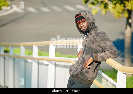 Serious handsome young man leaning on railing when resting after jogging in cold morning Stock Photo