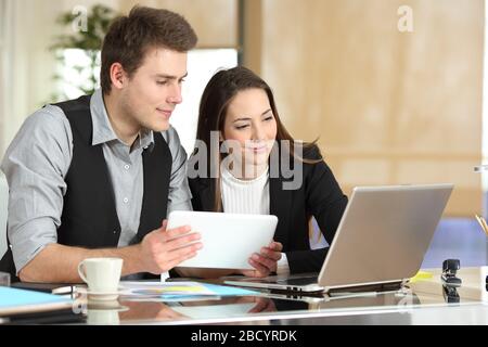 Two employees comparing tablet and laptop content sitting at office Stock Photo