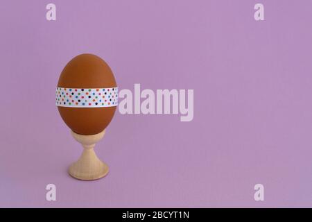 Egg standing on cup, on a soft purple background. Easter egg tied with a festive ribbon Stock Photo
