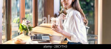 Banner of Portrait Young Asian woman holding and drinking a cup of coffee and working with technology laptop at a coffee shop.freelancer and entrepren Stock Photo