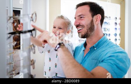 Young man and his cute daughter are choosing the best apropriate eyeglasses in ophthalmology clinic Stock Photo