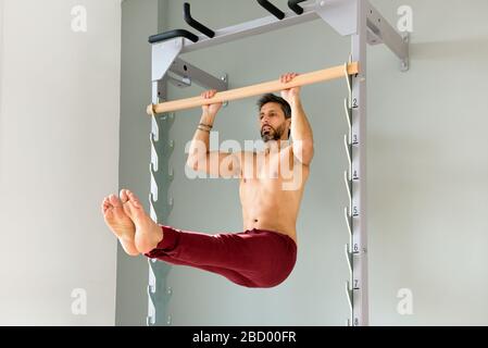 Muscular shirtless athletic man doing a pull up L sit in the hold