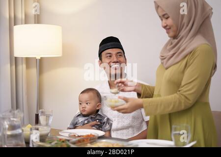 beautiful hijab woman serving some food for her husband during breaking the fast in the evening Stock Photo