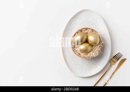 Easter elegant table setting with golden eggs in nest on white table. View from above. Space for text. Stock Photo