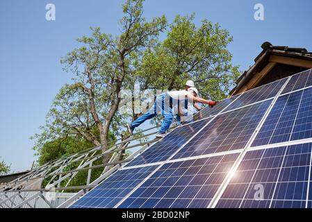 Bottom view of two technicians on metal platform installing solar photo voltaic panels on bright sunny day. Stand-alone solar panel system installation, efficiency and professionalism concept. Stock Photo