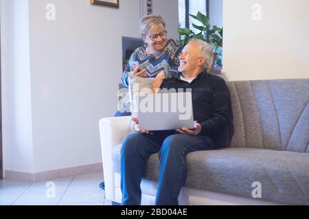 Retired senior people at home enjoying and use technology laptop computer during coronavirus lockdown quarantine time - elderly lifestyle with interne Stock Photo