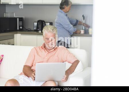 Elderly lifestyle people at home enjoying kitchen and desktop laptop computer - coronavirus lockdown quarantine emergency for old senior couple living Stock Photo