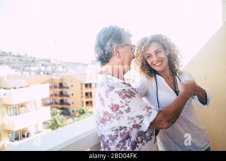 Two different ages women friends touch punch outdoor at home in the terrace with city view - concept of team and friendship or mother and daughter adu