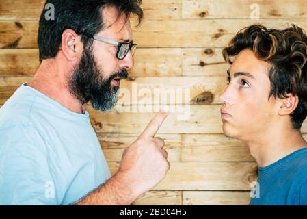 Adult caucasian man father telling out her teenager son at home - family portrait and education concept - generations and parentship - wooden backgrou Stock Photo