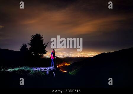 Lifeguard in red jacket with medical cross and beam of head light in the mountain ski resort with view to night city light Stock Photo