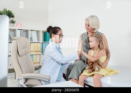 Smiling mature Asian pediatrician giving high five to little girl and congratulating her with recovery Stock Photo