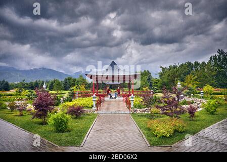 Young Couple in red checked shirts sitting and holding by hands in the Japanese Pagoda garden at rainy overcast sky Stock Photo