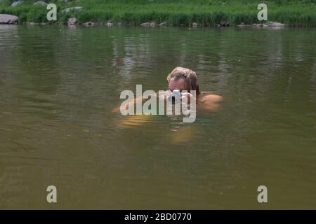 photographer holding camera swimming by river with just head above water trying to catch some interesting shots. Professional photographer job concept Stock Photo
