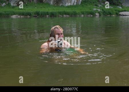 Mature caucasian man holding waterproof camera and swimming in river, trying to catch some interesting shots. Professional photographer job concept. W Stock Photo