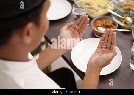young man with muslim cap pray open his arm before having the meal Stock Photo