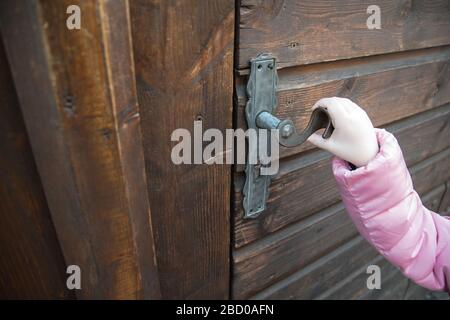 A little girl in pink jacket holding old metal door handle on the wood door in winter. Vintage iron pen. Stock Photo