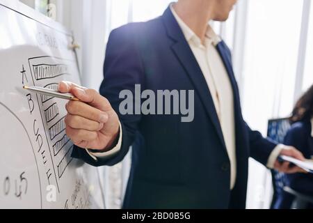 Close-up image of entrepreneur pointing at diagram on whiteboard when talking in front of colleagues about company development Stock Photo