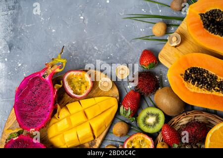 Set of exotic thai fruits over gray blue background. Fresh sliced papaya, kiwi, passion fruit, longan,strawberry on wooden cutting boards . Copy space Stock Photo