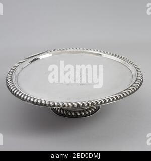 Footed Salver. Research in ProgressCylindrical foot, straight platter. Spreading base of foot and rim of top edged with repoussé cording. Engraved in center are three swords in lozenge shield, surrounded by feathers. “M.P.” engraved on back. Footed Salver Stock Photo