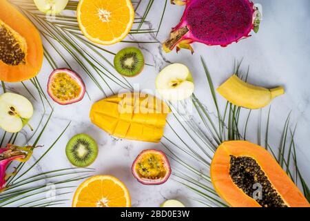 Fresh exotic fruits on light background. Halves of ripe papaya, mango, passion fruit, orange, dragon fruit on white marble table. Top view. Horizontal Stock Photo
