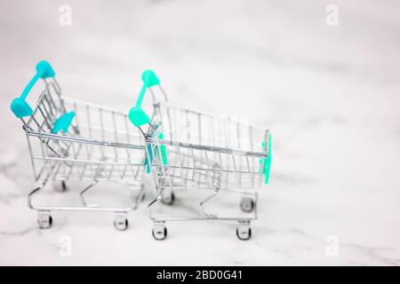 Two empty metal small miniature toy shopping trolley on white marble background. Shopping, supermarket, sale concept. Collection of shopping carts. Stock Photo