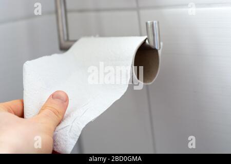 Man grabs toilet paper from an almost empty roll as a close up Stock Photo
