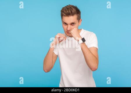 Fighting spirit. Portrait of confident handsome man in white t-shirt clenching fists in boxing gesture and bravely looking at camera, ready to punch. Stock Photo
