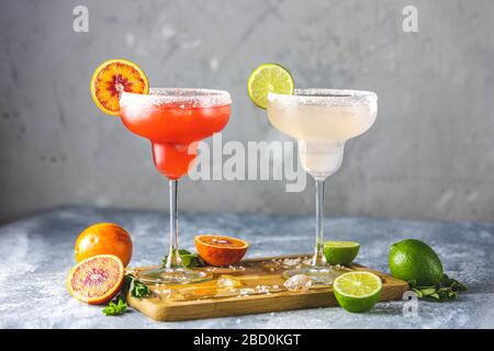 Frozen lime margarita and blood orange margarita cocktail mix in salt rimmed glasses garnished with slices of lime and orange. Focus on the citrus sli Stock Photo