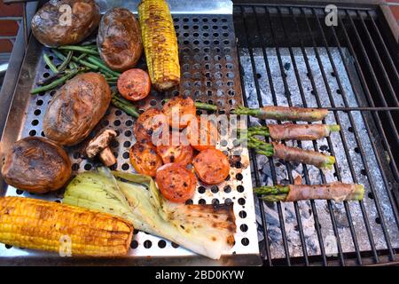 Side dishes on the barbecue Corn on the cob mushrooms green beans leeks tomatoes red potatoes asparagus wrapped in prosciutto ham on the outdoor grill Stock Photo
