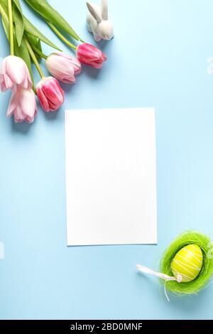 Bouquet pink tulips, bunny, easter nest and blank for cheers on blue. Spring. Happy Easter holiday. Greeting card. Vertical. Top view. Stock Photo