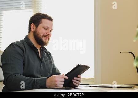 Male manager using tablet at office, laptop on desk. Stock Photo