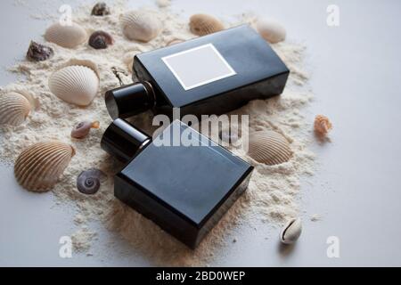 Two dark glass perfume bottles on sand with seashells Stock Photo