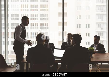 Silhouettes of people sitting at the table. A team of young businessmen working and communicating together in an office. Corporate businessteam and Stock Photo