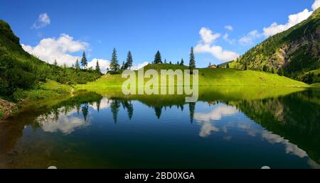 Mountain lake shore in sunlight and shadow symmetrically reflected in the clear blue water creates an almost surreal scenery Stock Photo